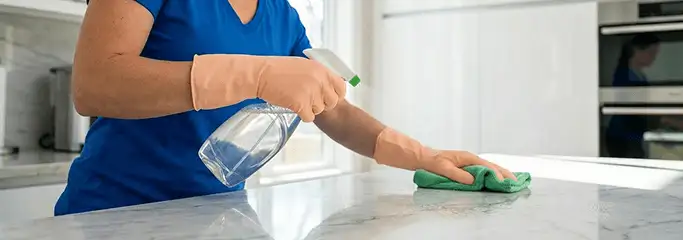 Maid service worker spraying and wiping a kitchen countertop with a microfiber cloth for sanitizing, Duluth, MN.