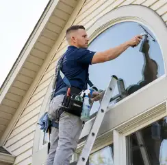 Professional window cleaner on a ladder using a squeegee to clean an exterior arched window, Duluth, MN.