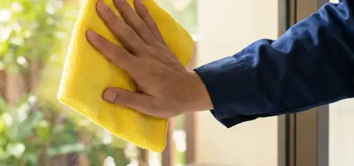 House cleaner wiping a glass window with a yellow microfiber cloth for streak-free cleaning, Duluth, MN.